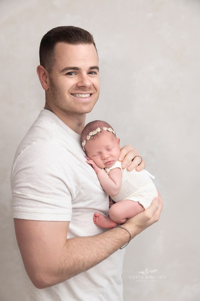 dad smiles proudly while cradling baby during a newborn photo session