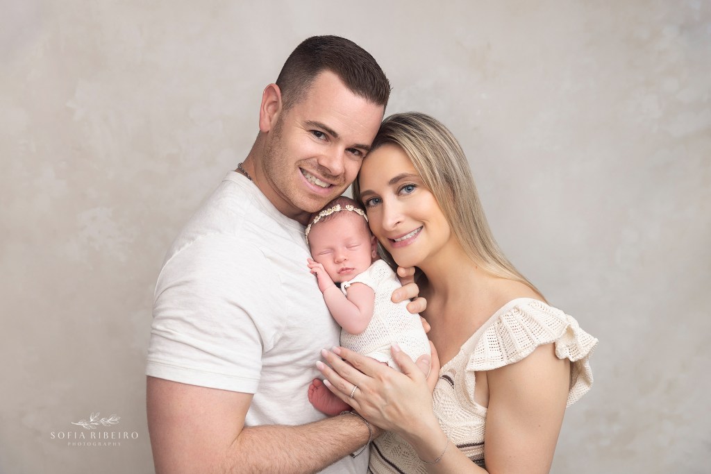 mom and dad smile to the camera with a sleepy newborn girl for portraits with a monroe nj newborn photographer
