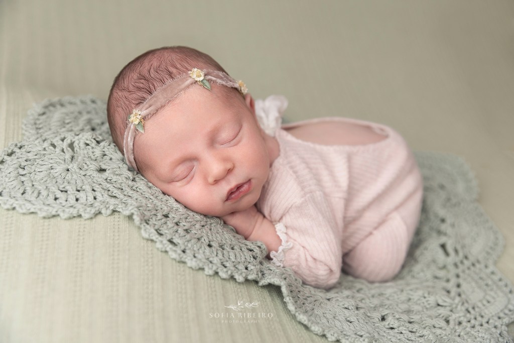baby girl lies on top of a mint green knit fabric, in a pink outfit during a photo session with a monroe nj newborn photographer