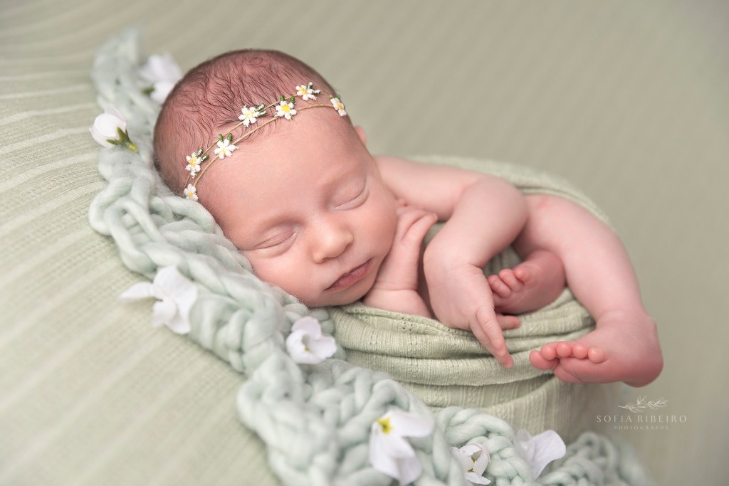 baby girl wears a daisy headband and is wrapped in green, sleeping soundly
