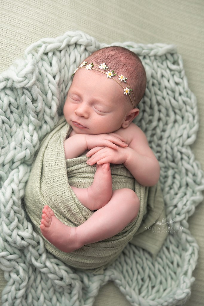 baby girl wears a daisy headband and is wrapped in green, sleeping soundly