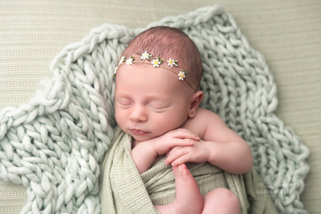 baby girl wears a daisy headband and is wrapped in green, sleeping soundly