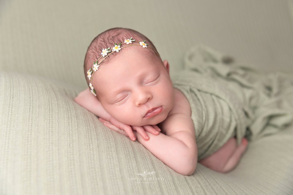 baby girl wears a daisy headband and is wrapped in green, sleeping soundly, posed on her hands, face to camera