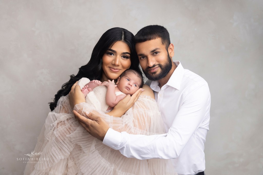 mom and dad smile to camera, wearing neutral tones during their family photos with their new baby boyo