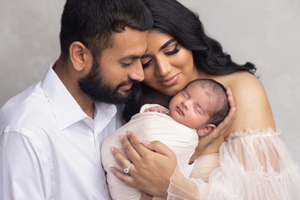 mom and dad hold their sweet baby close as he smiles sweetly in his sleep in staten island ny