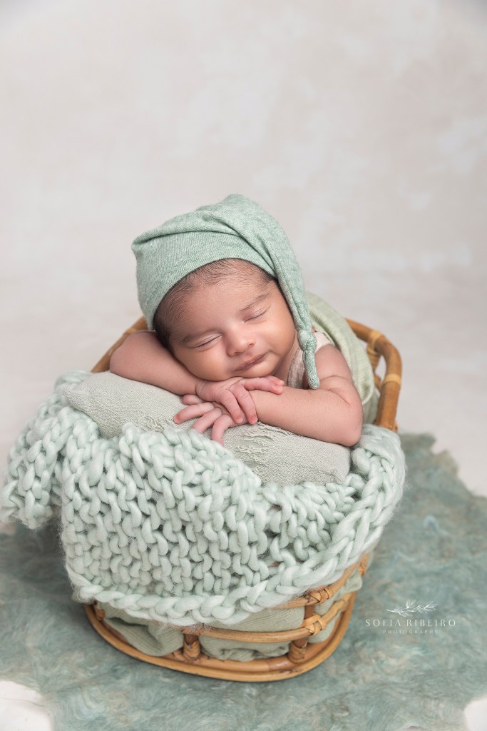 baby smiles while posed in a sleepy cap inside a crate during newborn photos