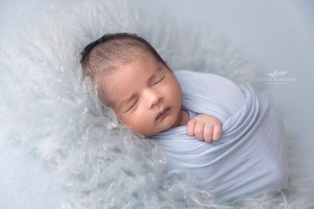 baby is sweetly wrapped in blue over a soft fur, during his newborn photos