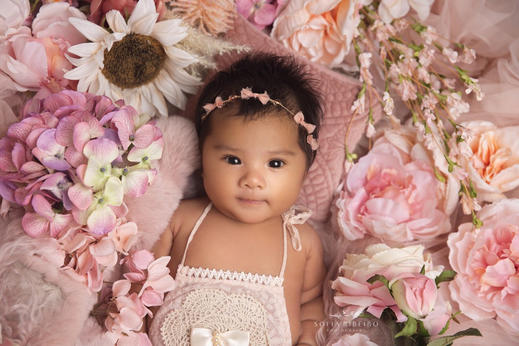 baby girl B smiles at the camer during newborn photos, snuggled in a bed of flowers