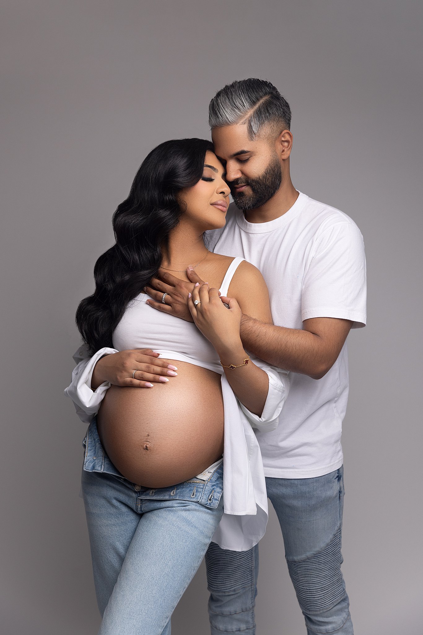 Happy expecting parents snuggle in white shirts and jeans after visiting view a miracle