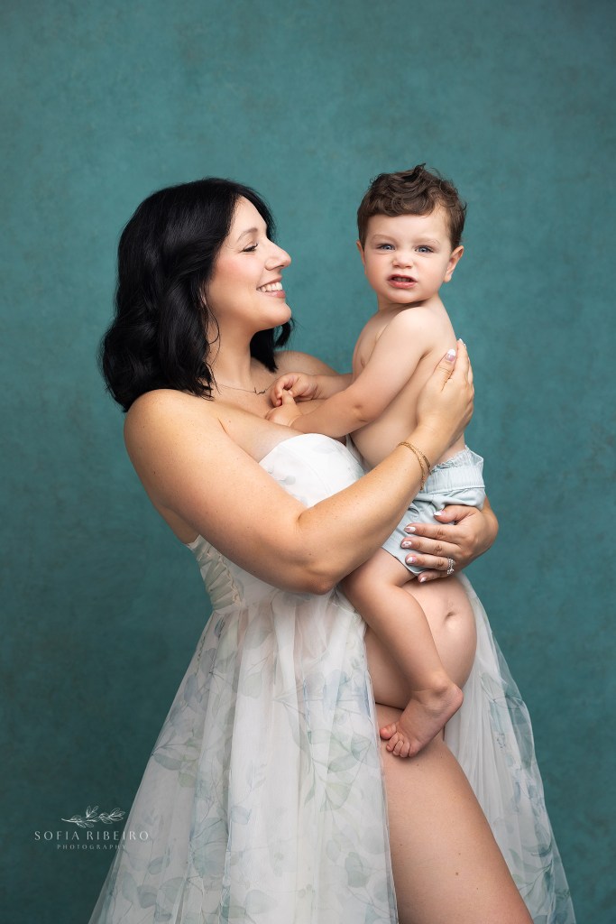 mom cradles big brother over her belly for maternity portraits, while big brother makes a silly face