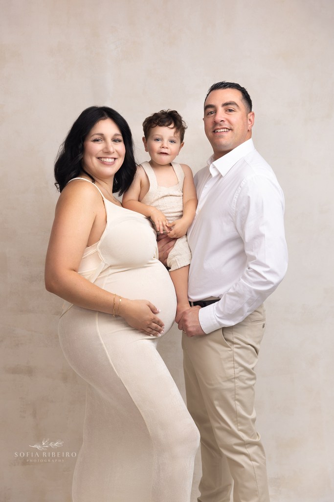 a soon to be family of four poses together smiling at the camera