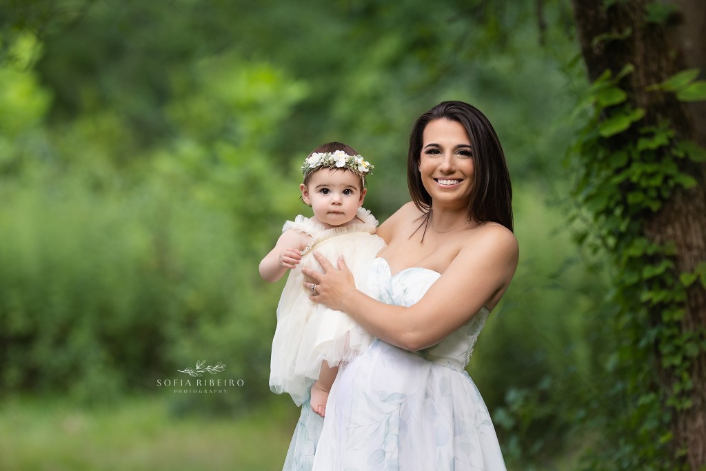 mom holds her baby girl in matching outfits against a background of forest greenery