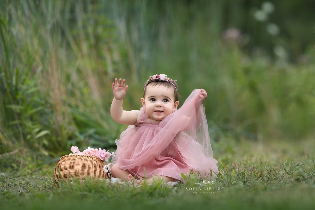 baby girl smiles in a pink dress sitting in a field outdoors for photos