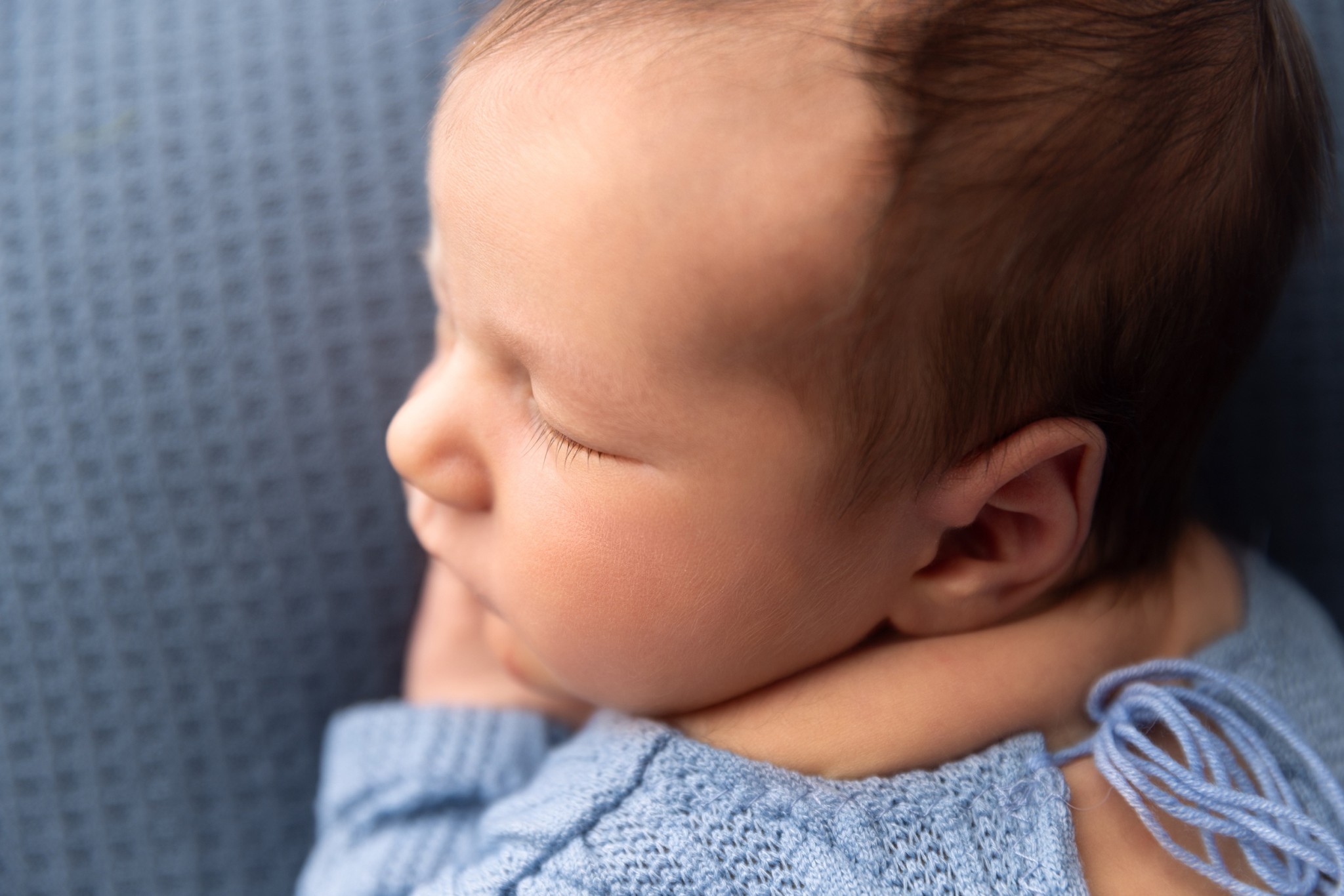 Details of a sleeping newborn baby's face in a blue knit onesie