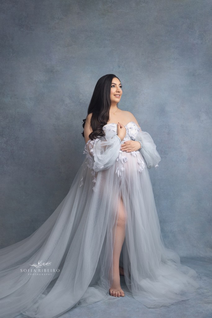 a mom poses in a blue dress before taking a photo for her maternity session
