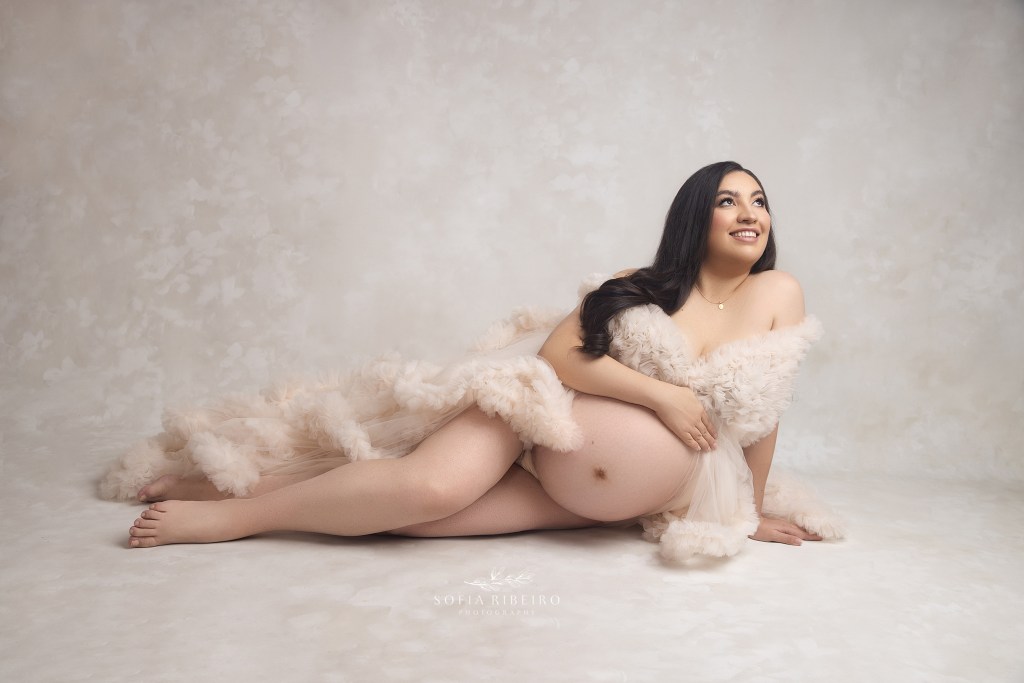 mom is a dream in a ruffled cream gown with her hand gently resting on her belly for a maternity photo