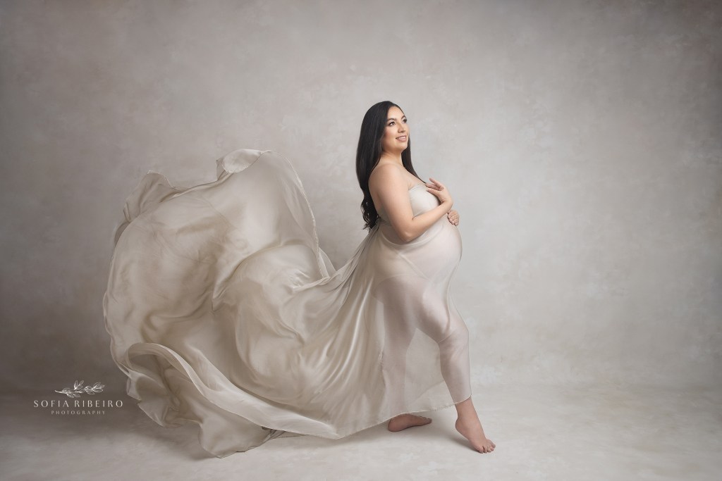 mom wears a flowing neutral fabric, wrapped around her baby bump during a photo session in hackensack nj with a maternity photographer