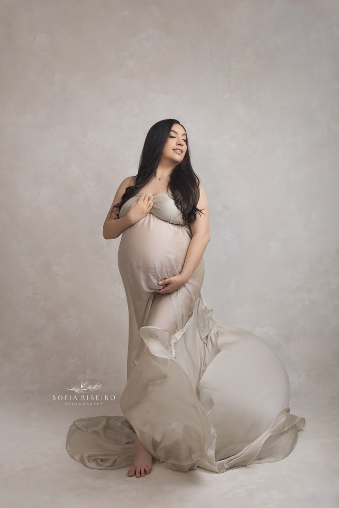 mom wears a flowing neutral fabric, wrapped around her baby bump during a photo session in hackensack nj with a maternity photographer