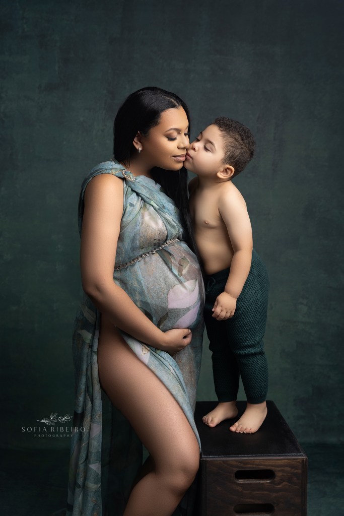 big brother gives his mom a sweet kiss while cradling her baby bump