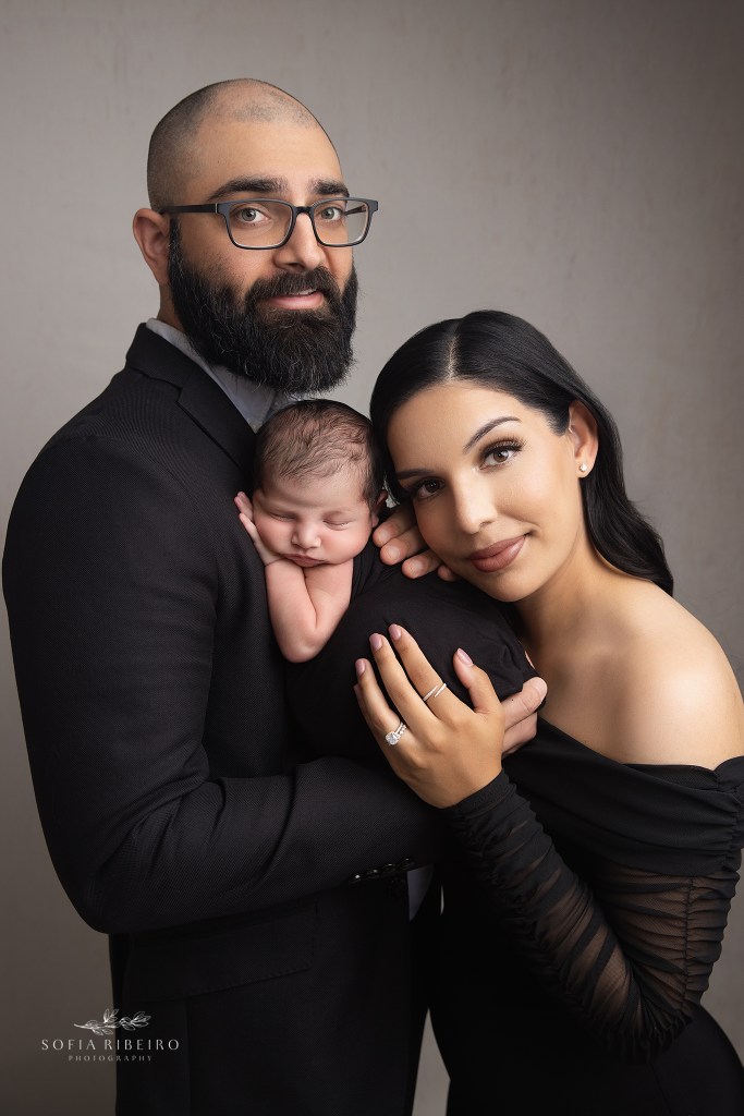 dad and mom snuggle together with a new baby during a photo session, both wearing black