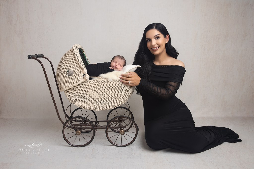 posed newborn baby in a carriage prop with mom and big sister, with black outfits on