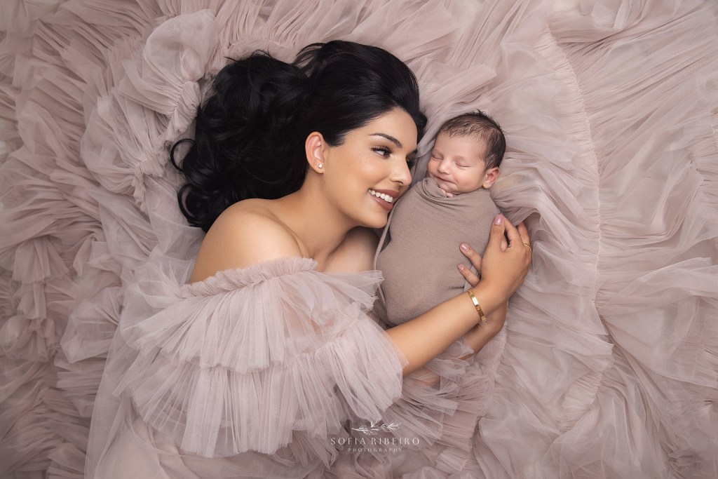 mom smiles adoringly at her new baby boy wrapped in a taupe fabric in a bed of tulle