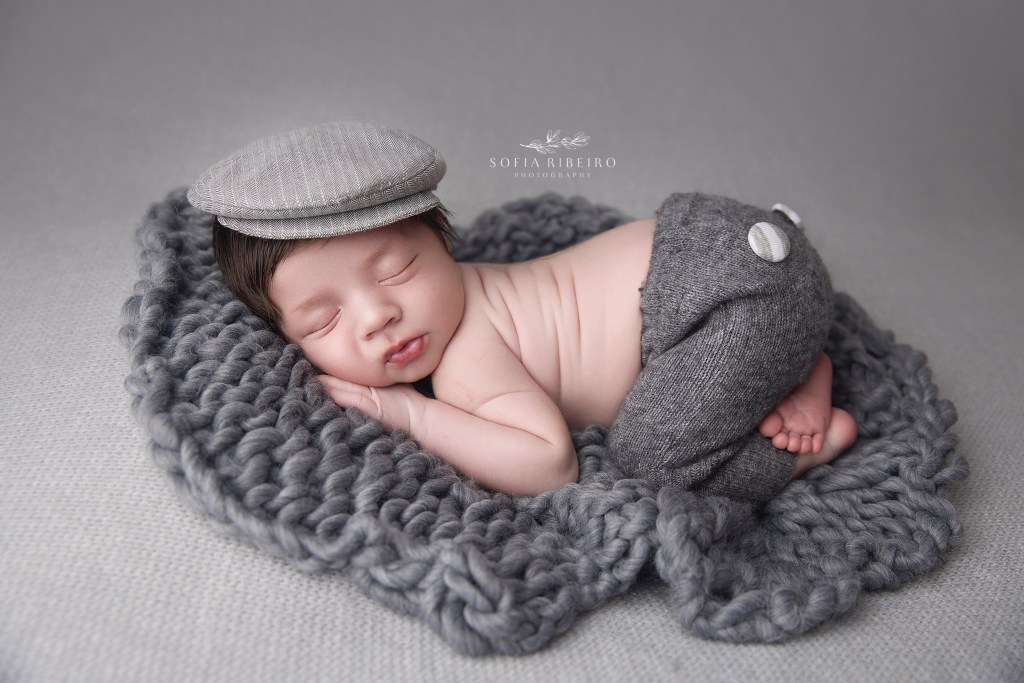 newborn baby is posed on his belly in a grey outfit for photos