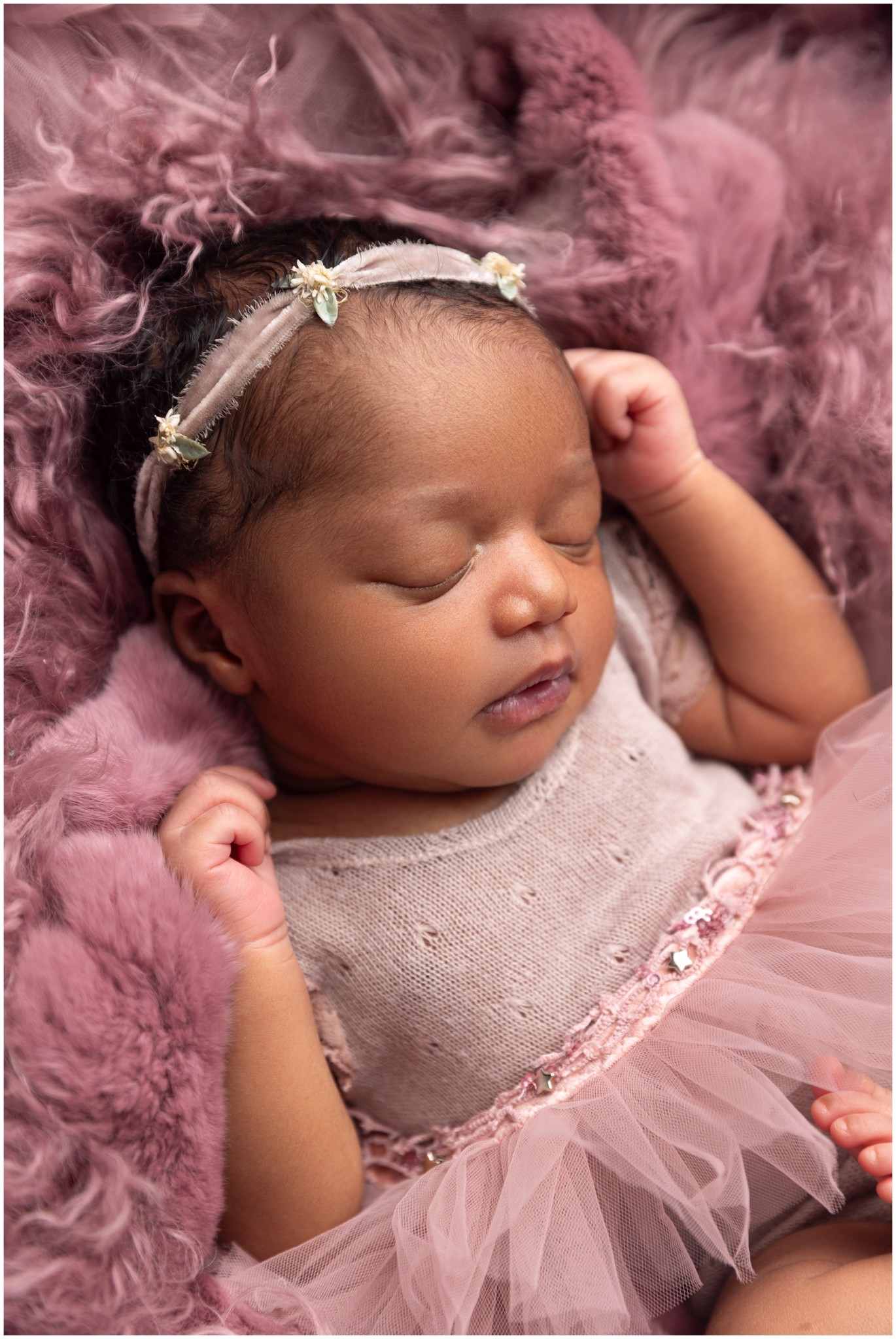 A newborn baby girl in a purple dress and tutu with matching headband