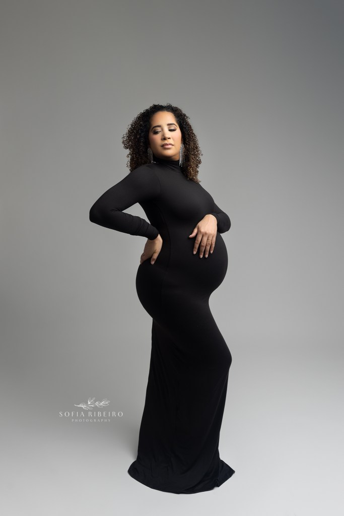mom looks to her left while cradling her baby bump for maternity portraits in a form fitting black dress