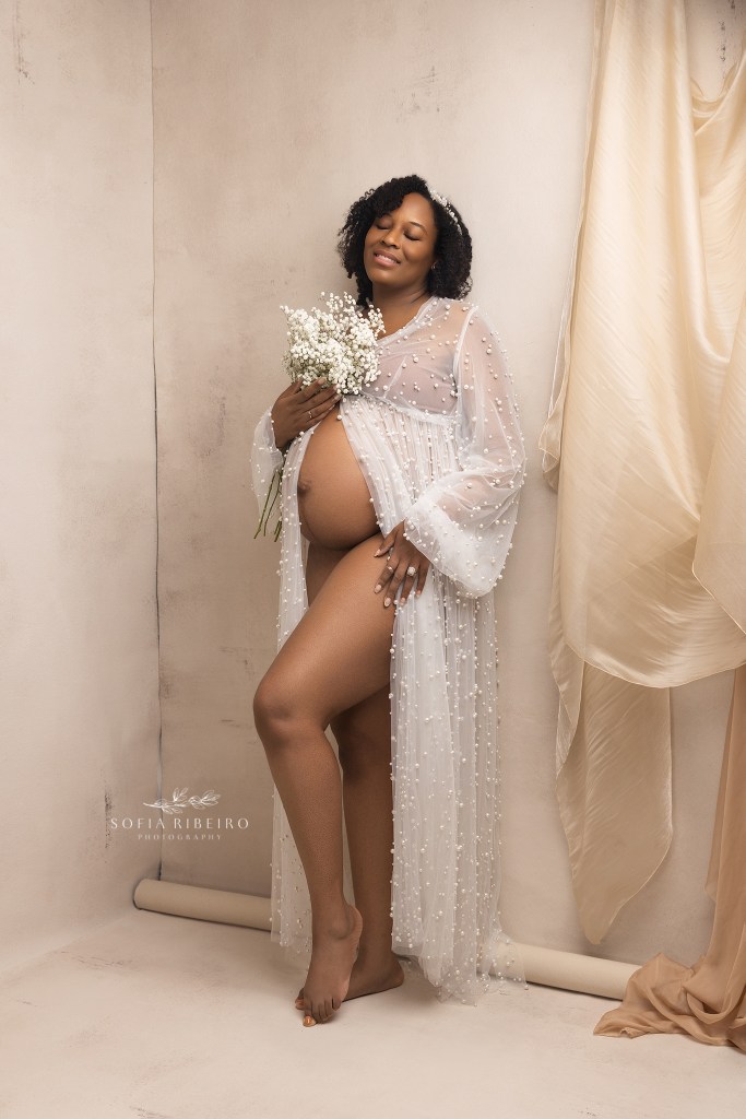 mom poses in a pearl dress with belly exposed against a neutral backdrop draped in fabric, during a photo session with a union city nj maternity photographer