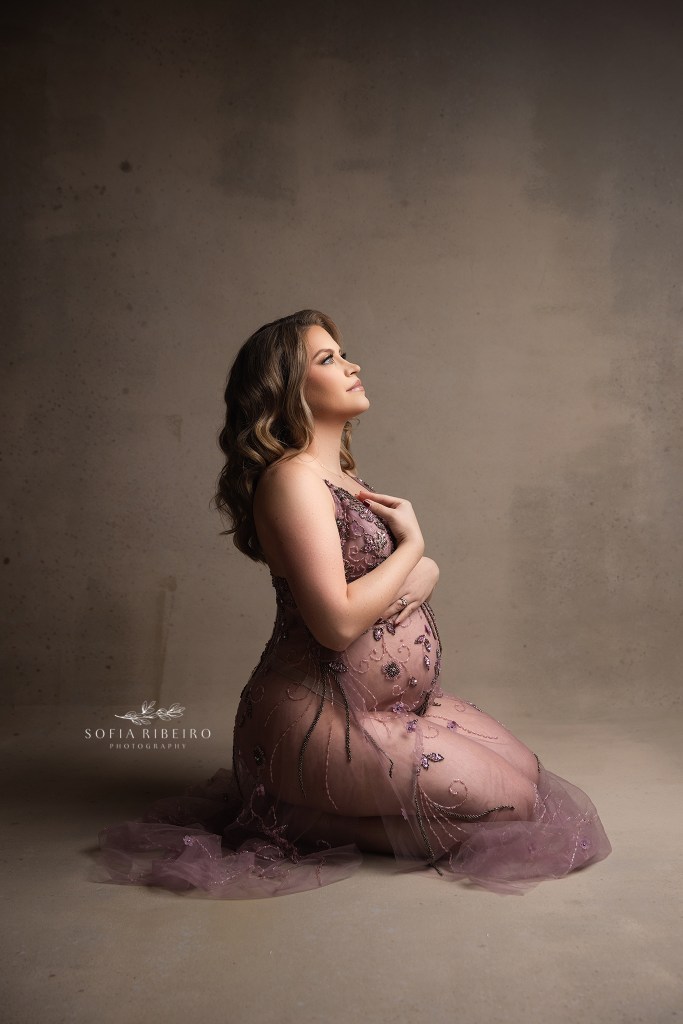 mom poses with hands on her heart for a seated maternity portrait