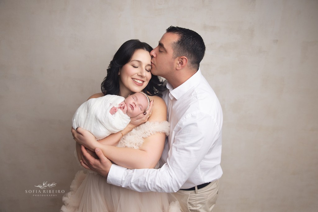 dad kisses mom on the forehead while snuggling with their new baby for newborn photos in bernard nj
