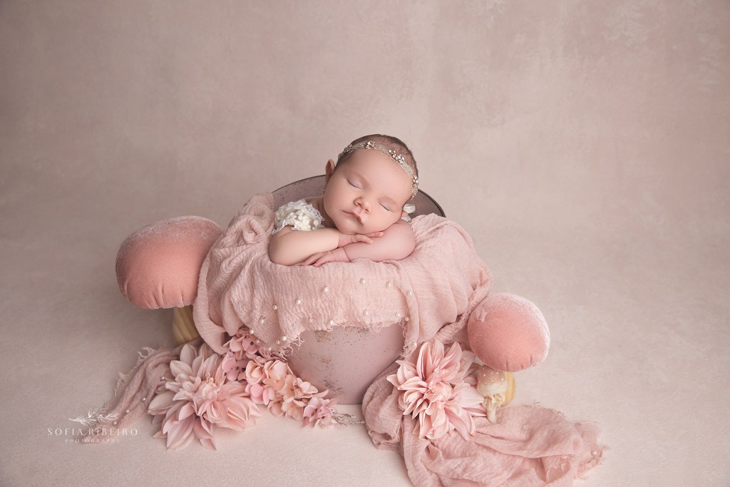 a soft pink backdrop with baby posed in a matching color bucket prop during a newborn photo session in bernards, nj