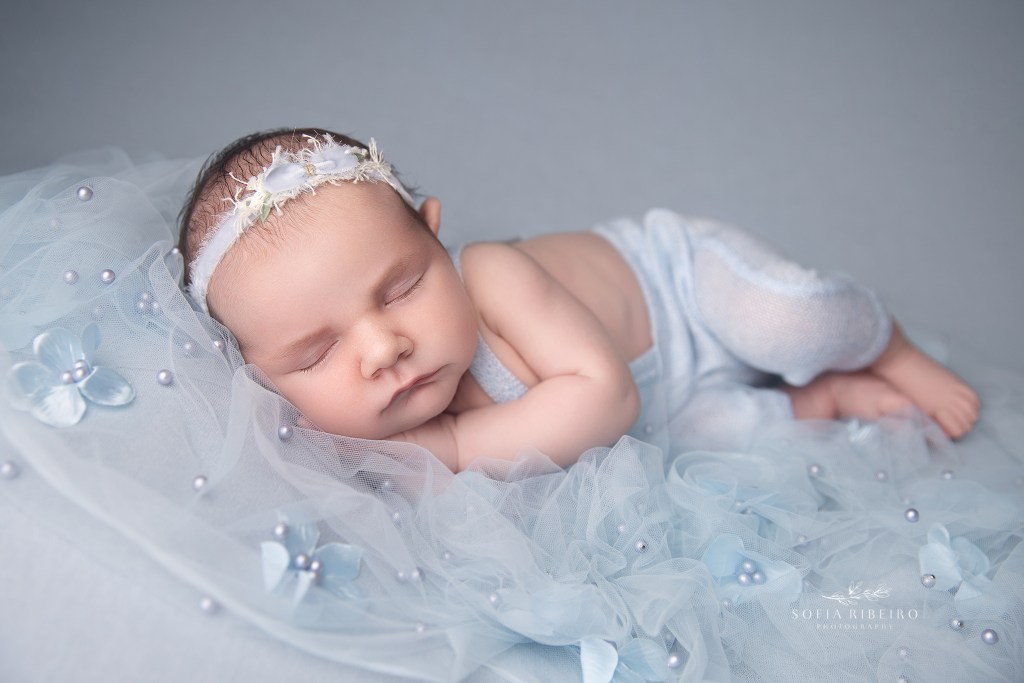 a newborn baby girl wearing light blue on a pale blue backdrop