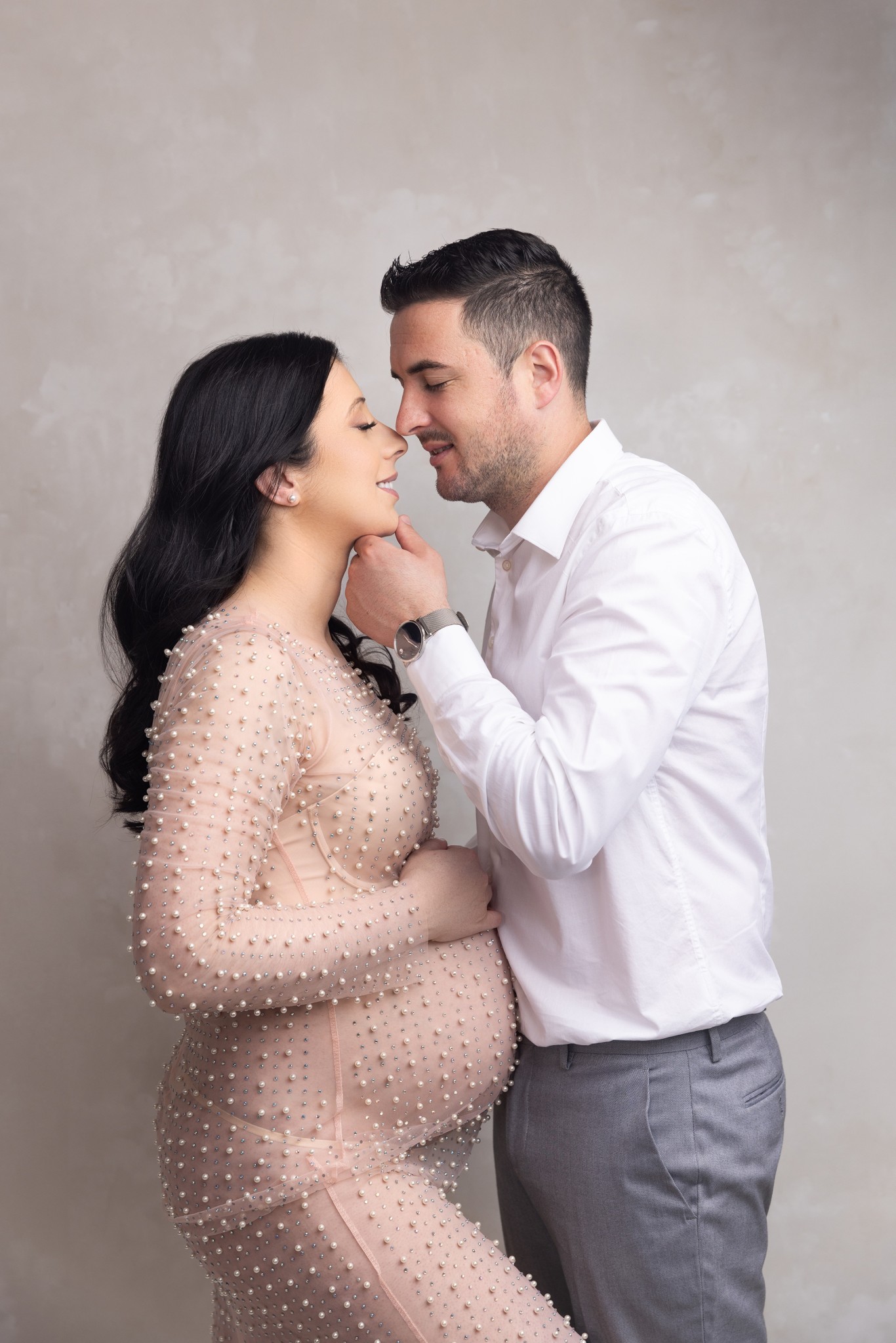 A mom to be leans in for a kiss while standing in a pink maternity gown with her husband after some prenatal yoga jersey city