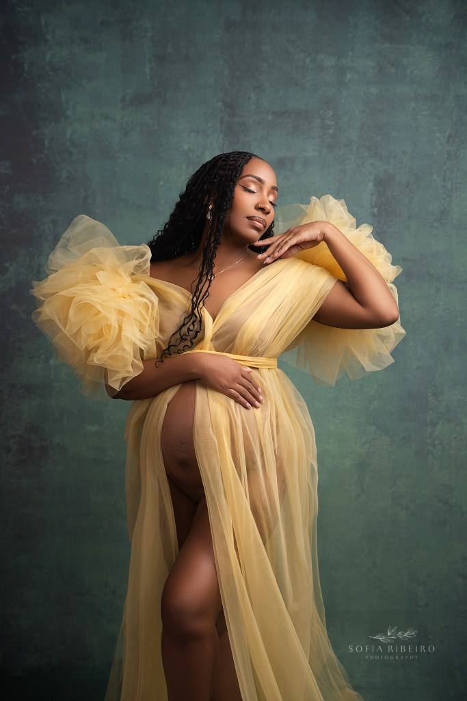 an nj maternity photographer in somerville nj dresses mom in a yellow tulle dress against a teal backdrop for a portrait