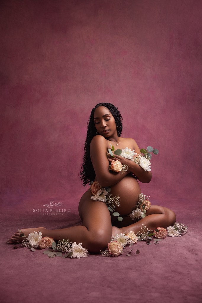 mom poses in a semi nude look against a purple background, adorned with florals in somerville nj showcasing her pregnancy
