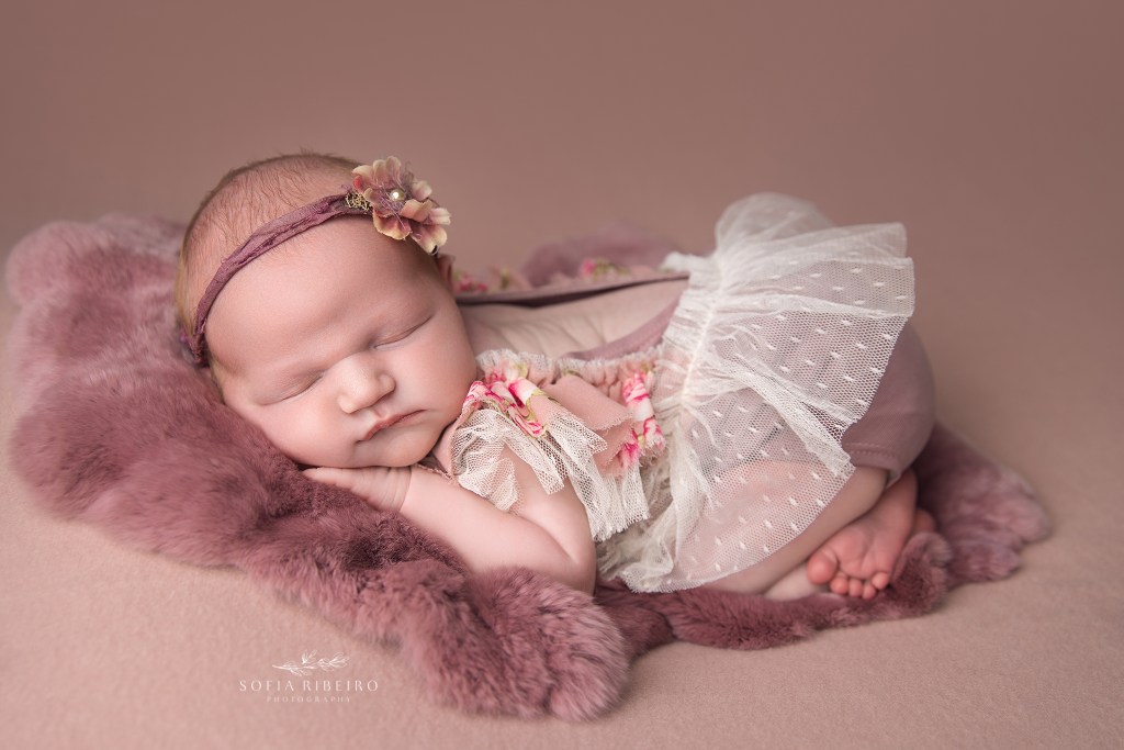newborn baby girl posed on a pink backdrop in a pink floral dress for a south plainfield nj newborn photographer