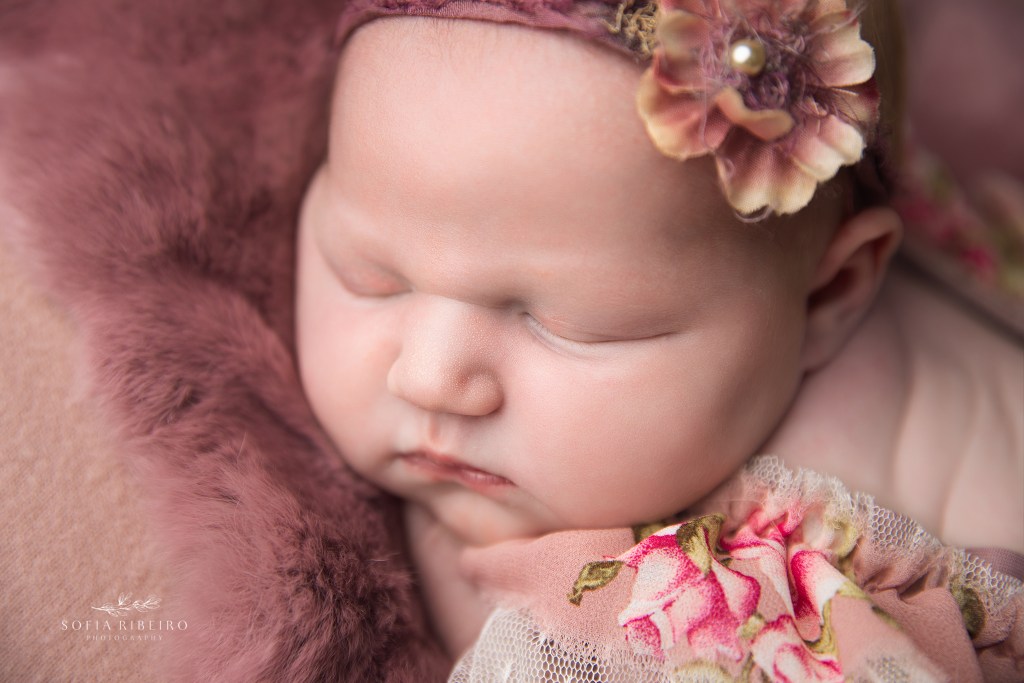 newborn baby girl posed on a pink backdrop in a pink floral dress for a south plainfield nj newborn photographer