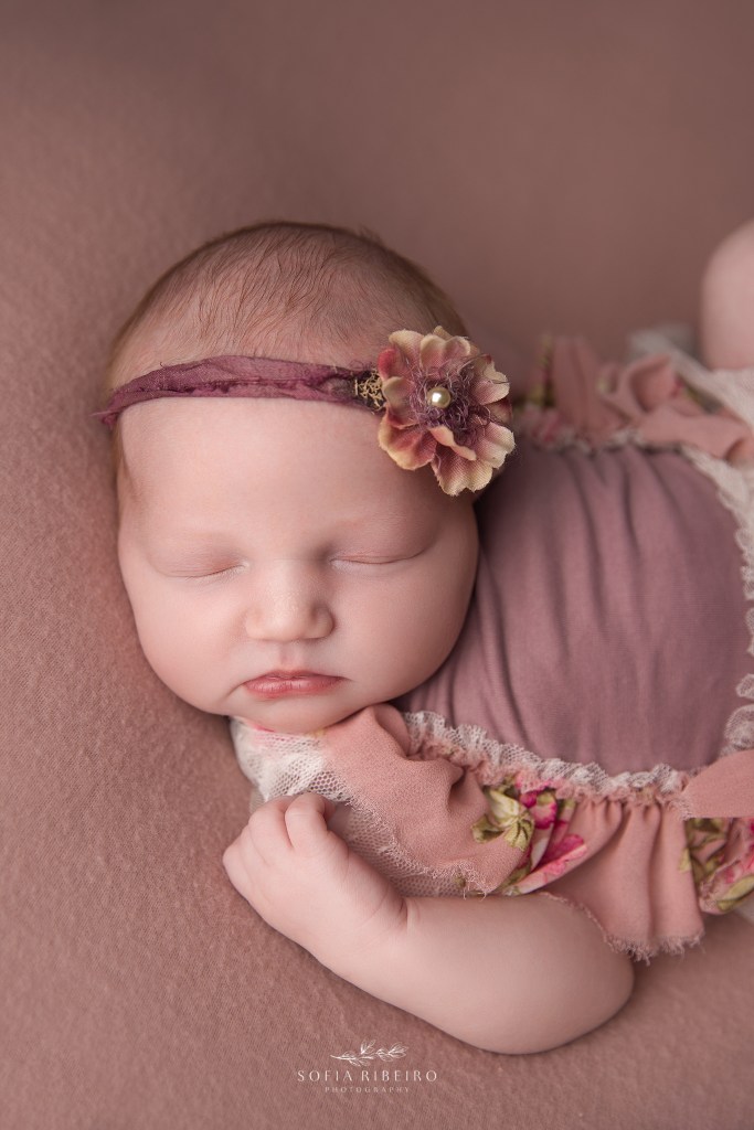 newborn baby girl posed on a pink backdrop in a pink floral dress for a south plainfield nj newborn photographer