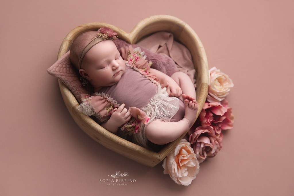 baby girl is posed in a heart shaped prop for a photo