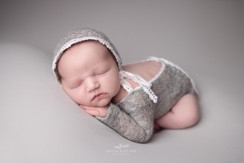 a baby girl is dressed in a light grey outfit and posed in a sleeping position
