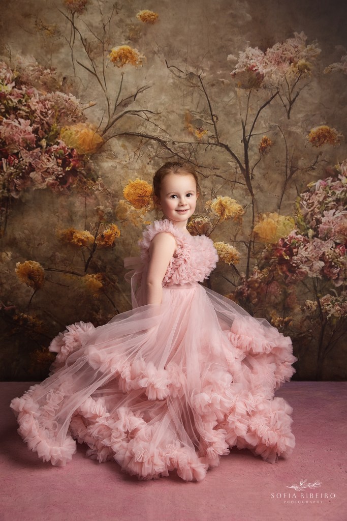 a gorgeous portrait of a 4 year old in a poufy pink princess dress against a floral backdrop