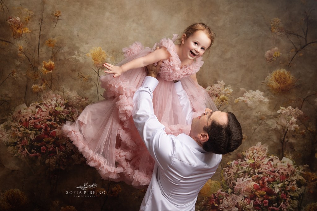 dad lovingly swirls with his little girl in the air in a pink poufy dress for a portait