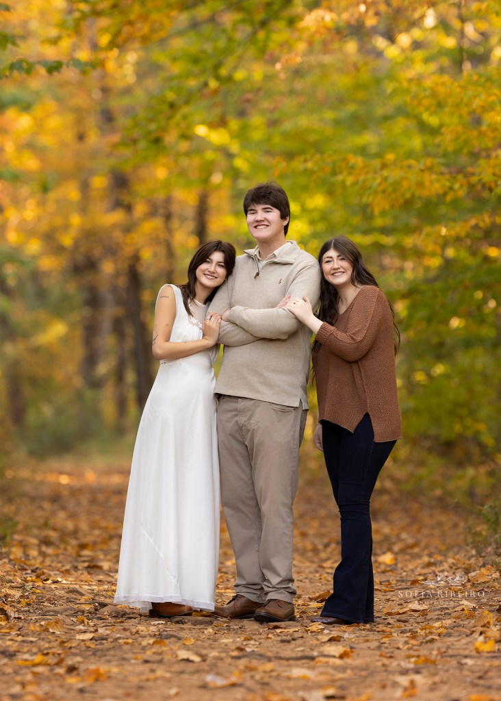 three grown siblings pose together in coordinating outfits in a park during the fall season in warren nj for family photos