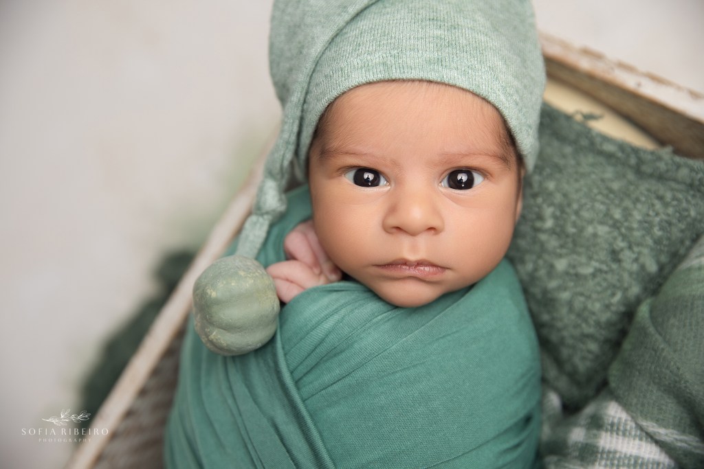 a newborn baby boy stares deeply into the camera, wrapped in green