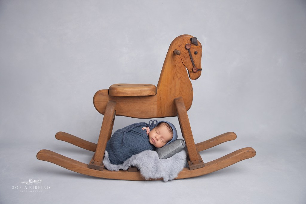a nj newborn photographer poses a baby under a prop rocking horse for a sweet image
