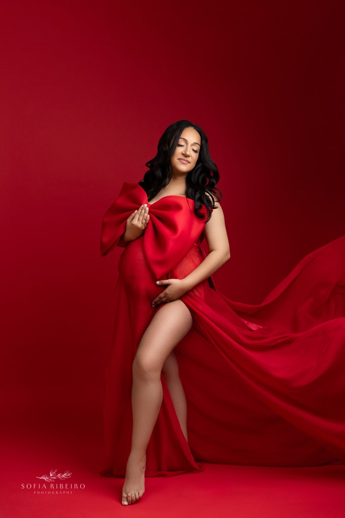 mom wears a red dress with a big bow draped over her baby bump for maternity portraits in belleville nj