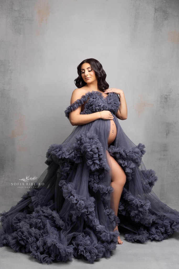 mom is posed elegantly in a maternity gown of grey ruffles with belly exposed for maternity portraits in colonia nj