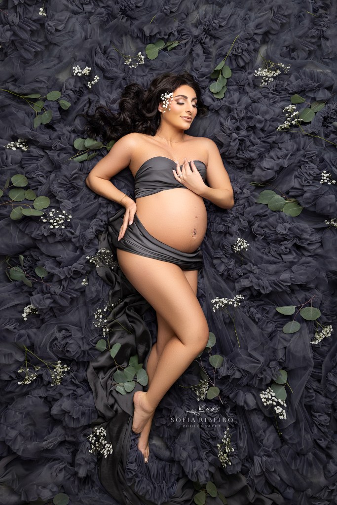 pregnant mom poses in a bed of grey tulle and flowers for a colonia nj maternity photographer